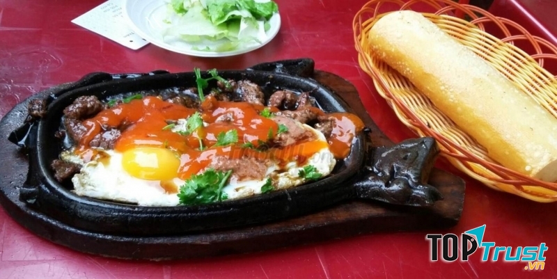 Miếng thịt bò để nguyên tảng, tẩm ướp đậm đà, chín mềm ngọt mà vẫn có vị ngọt tự nhiên, thêm trứng ốp la, pate thịt mềm mại, và vài lát chả lụa dai mềm. Ăn cùng với đó là ít rau mùi, dưa chuột, xà lách và bánh mì.