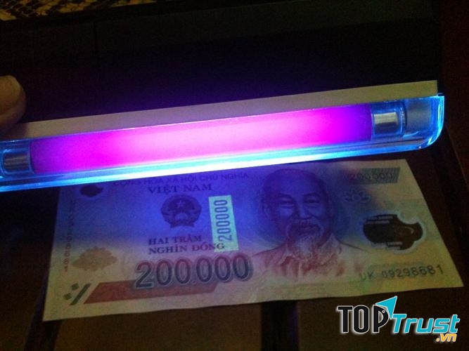 Soi tờ tiền dưới nguồn sáng để phân biệt